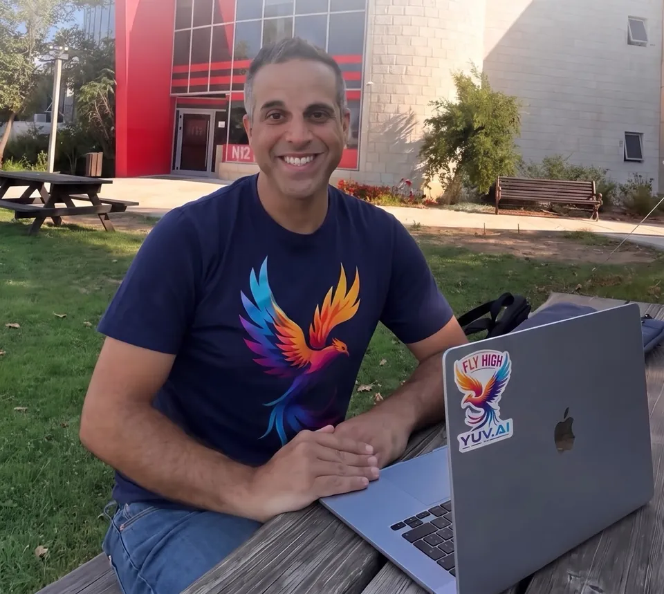 יובל אבידני מחייך ליד הלפטופ, מול בניין חדשות 12